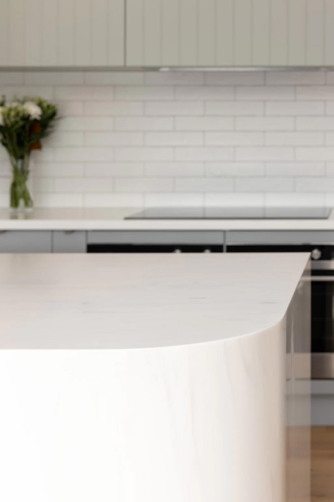 Inspiration for a large contemporary galley open plan kitchen in Auckland with a double-bowl sink, solid surface benchtops, white splashback, ceramic splashback, stainless steel appliances, medium hardwood floors, with island and white benchtop.
