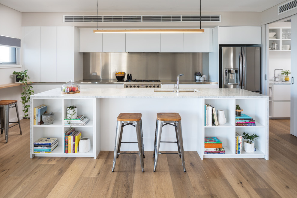 Photo of a contemporary single-wall open plan kitchen in Perth with flat-panel cabinets, white cabinets, marble benchtops, stainless steel appliances, with island, white benchtop, a double-bowl sink, metallic splashback, light hardwood floors and beige floor.