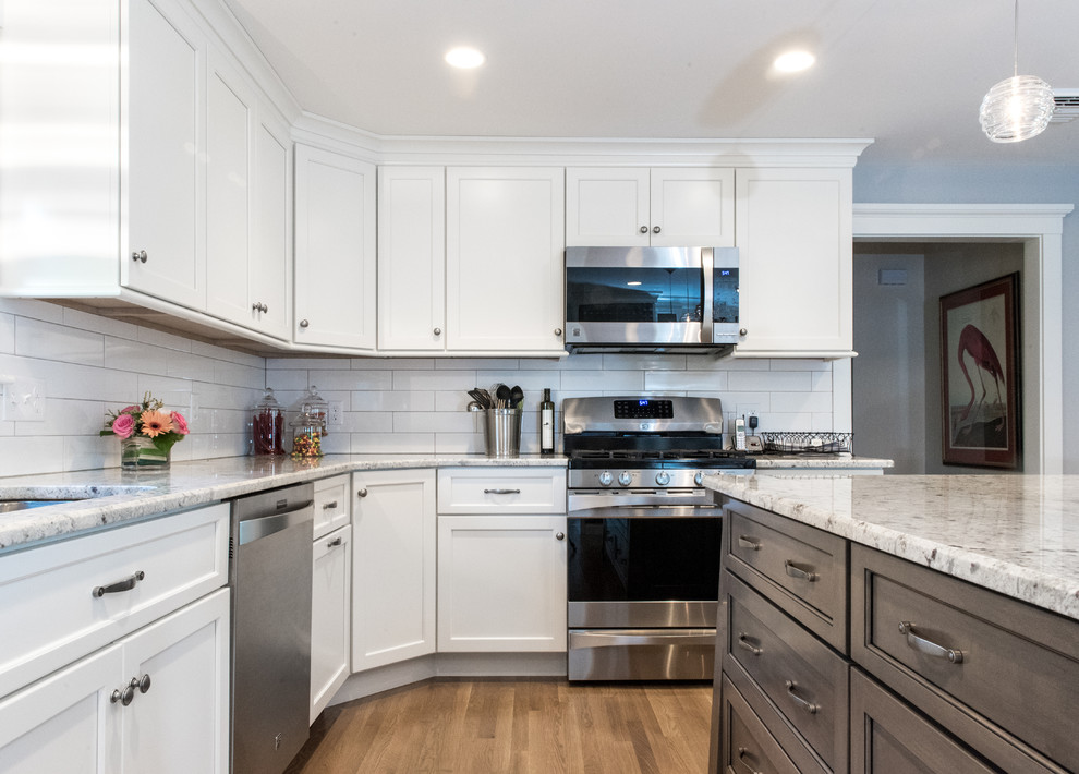 Photo of a large traditional u-shaped eat-in kitchen in Providence with a double-bowl sink, recessed-panel cabinets, white cabinets, granite benchtops, white splashback, ceramic splashback, stainless steel appliances, medium hardwood floors and with island.