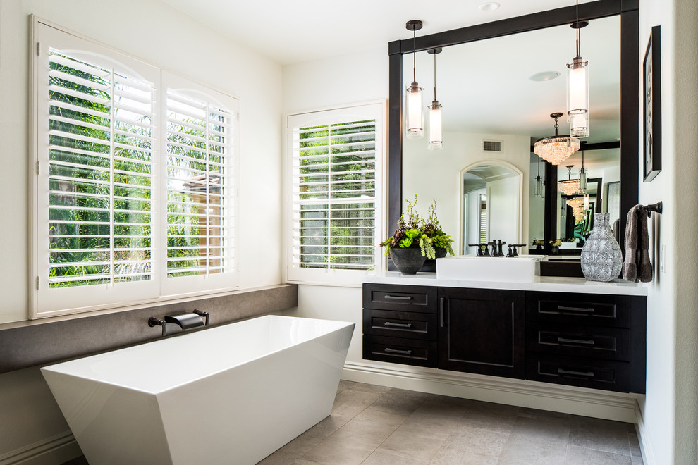 This is an example of a transitional master bathroom in Orange County with shaker cabinets, black cabinets, a freestanding tub, white walls, a vessel sink and grey floor.