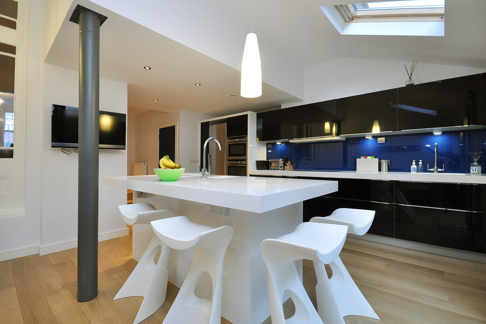 This is an example of a contemporary kitchen in London with flat-panel cabinets, black cabinets, blue splashback and stainless steel appliances.