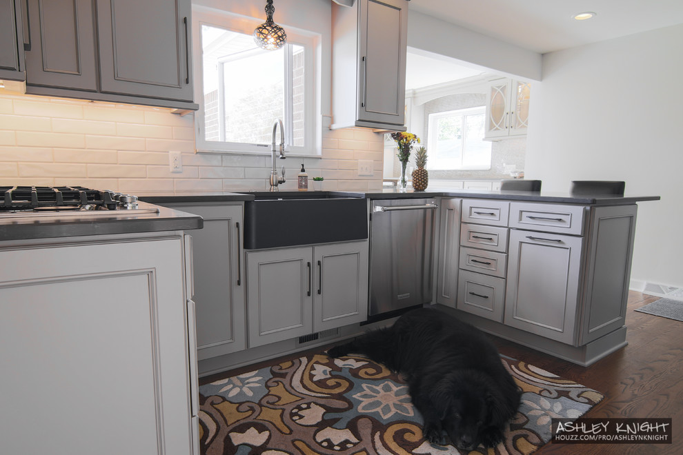 Mid-sized transitional u-shaped eat-in kitchen in Detroit with a farmhouse sink, recessed-panel cabinets, grey cabinets, quartz benchtops, white splashback, ceramic splashback, stainless steel appliances, medium hardwood floors, a peninsula, brown floor and grey benchtop.