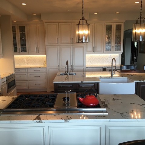 Example of a mid-sized transitional u-shaped medium tone wood floor kitchen design in Denver with a farmhouse sink, raised-panel cabinets, white cabinets, marble countertops, white backsplash, stone tile backsplash, paneled appliances and an island
