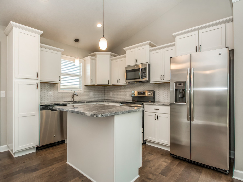 Example of a large transitional medium tone wood floor and brown floor eat-in kitchen design with an undermount sink, shaker cabinets, white cabinets, granite countertops, white backsplash, subway tile backsplash, stainless steel appliances, an island and multicolored countertops