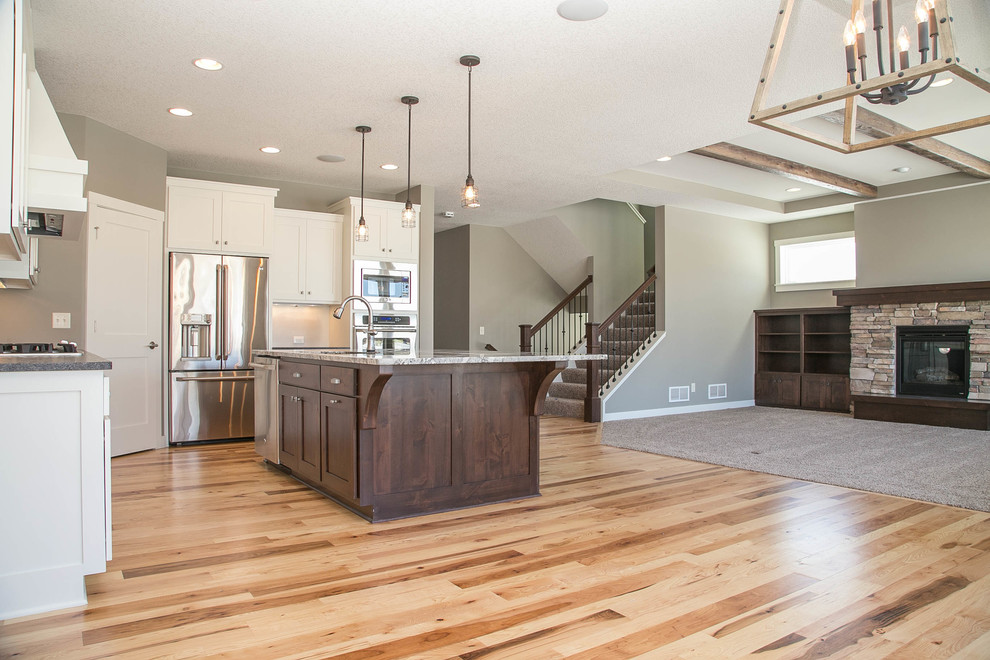 This is an example of an expansive country l-shaped open plan kitchen in Minneapolis with an undermount sink, shaker cabinets, white cabinets, granite benchtops, white splashback, subway tile splashback, stainless steel appliances, medium hardwood floors and with island.