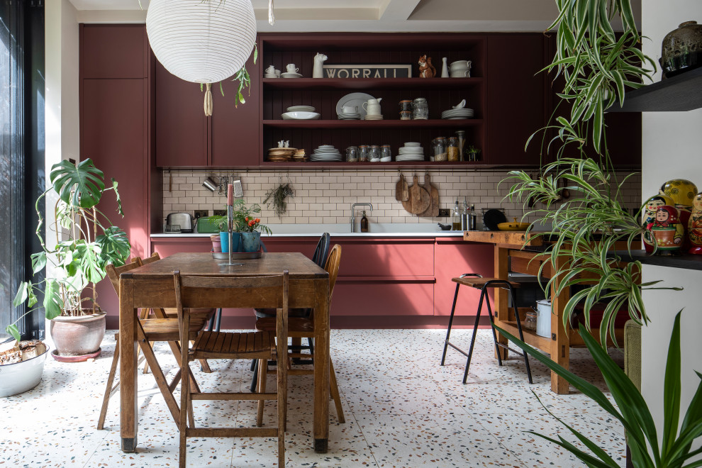 На фото: кухня в стиле фьюжн с обеденным столом, плоскими фасадами, красными фасадами, розовым фартуком, фартуком из плитки кабанчик, островом, разноцветным полом и белой столешницей с
