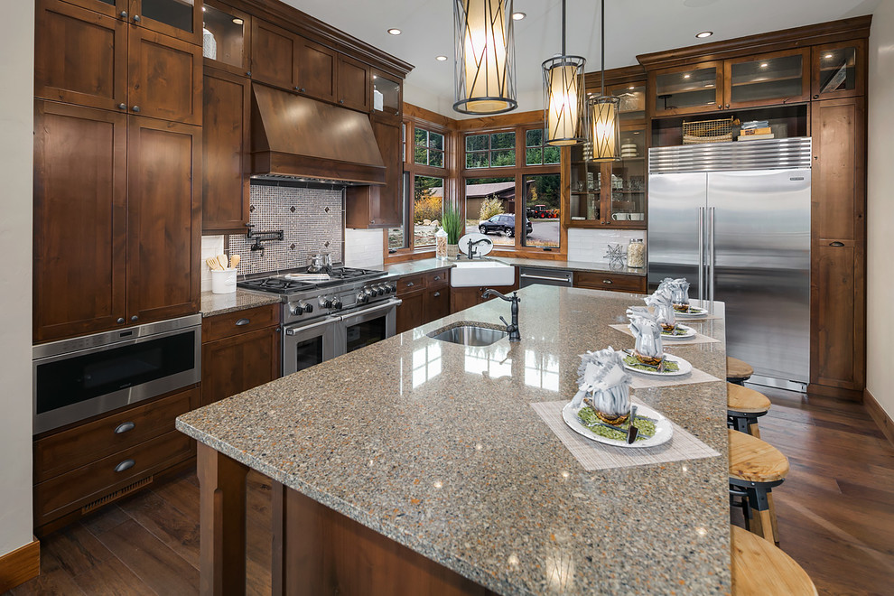 Example of a mountain style l-shaped dark wood floor kitchen design in Seattle with a farmhouse sink, shaker cabinets, dark wood cabinets, granite countertops, white backsplash, subway tile backsplash, stainless steel appliances and an island
