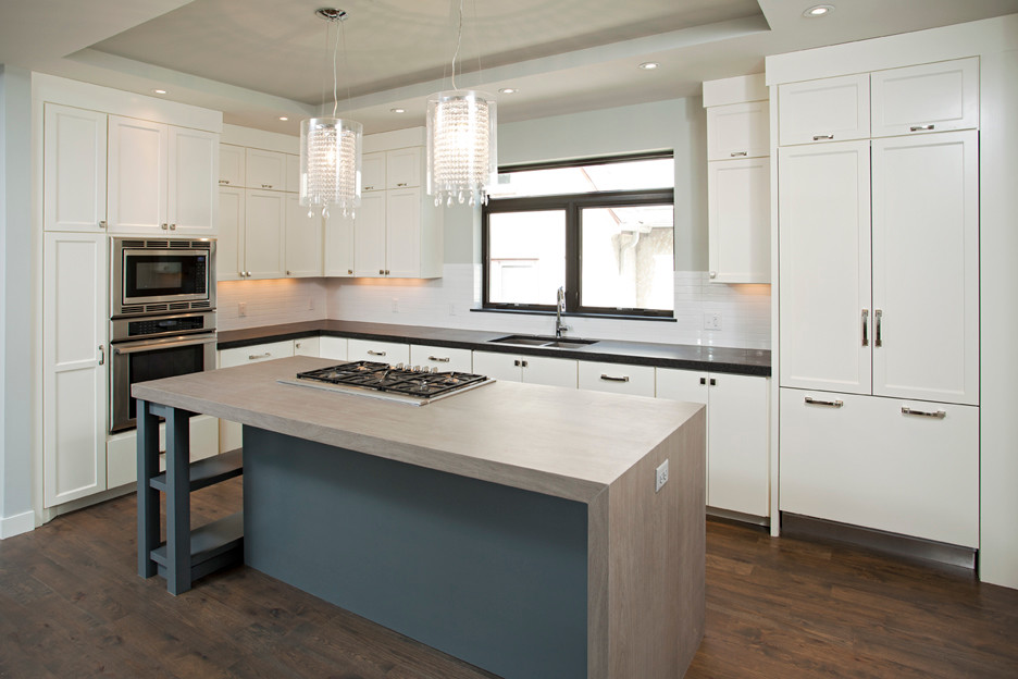 Mid-sized modern l-shaped open plan kitchen in Minneapolis with a double-bowl sink, shaker cabinets, white cabinets, solid surface benchtops, white splashback, porcelain splashback, stainless steel appliances, medium hardwood floors and with island.