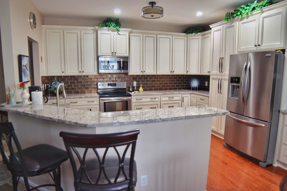 Example of a mid-sized u-shaped medium tone wood floor and brown floor kitchen design in Charleston with an undermount sink, raised-panel cabinets, beige cabinets, granite countertops, brown backsplash, ceramic backsplash, stainless steel appliances and beige countertops