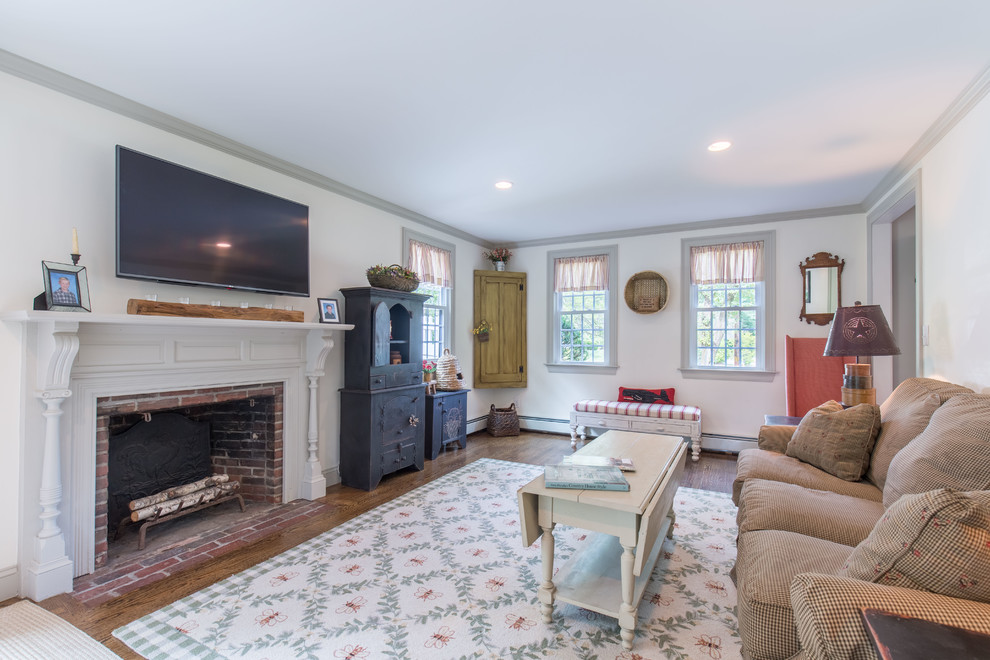 Photo of a traditional enclosed living room in Boston with white walls, dark hardwood floors, a standard fireplace, a brick fireplace surround, a wall-mounted tv and brown floor.