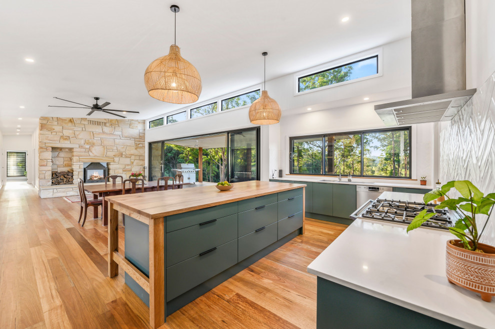Design ideas for a world-inspired l-shaped open plan kitchen in Melbourne with a submerged sink, flat-panel cabinets, green cabinets, white splashback, stainless steel appliances, medium hardwood flooring, an island, brown floors and white worktops.
