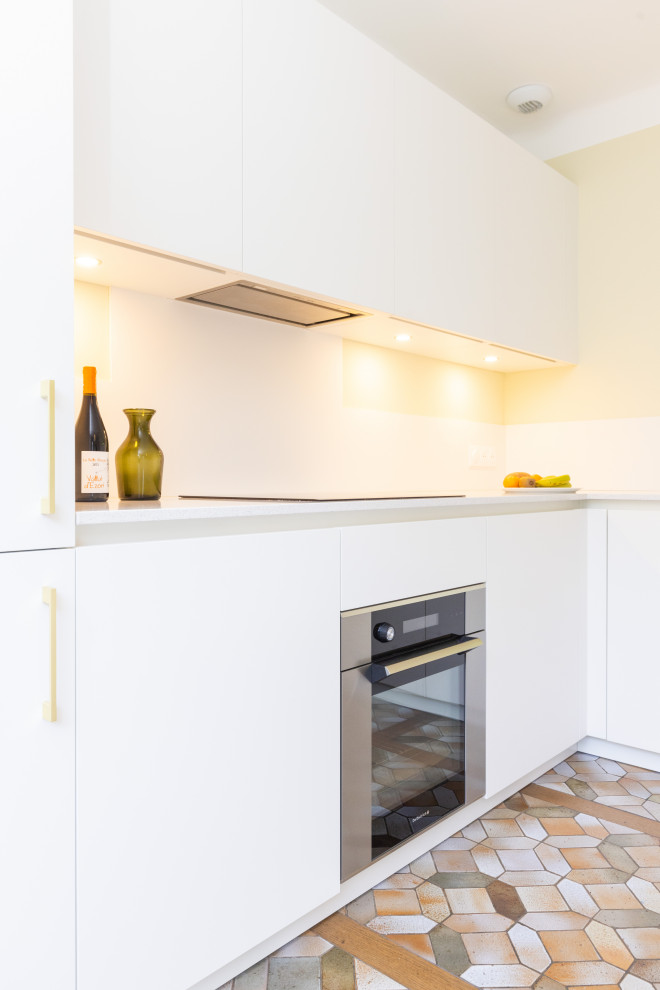 This is an example of a large modern l-shaped open plan kitchen in Nancy with an undermount sink, flat-panel cabinets, white cabinets, quartzite benchtops, white splashback, panelled appliances, terrazzo floors, with island, brown floor and white benchtop.