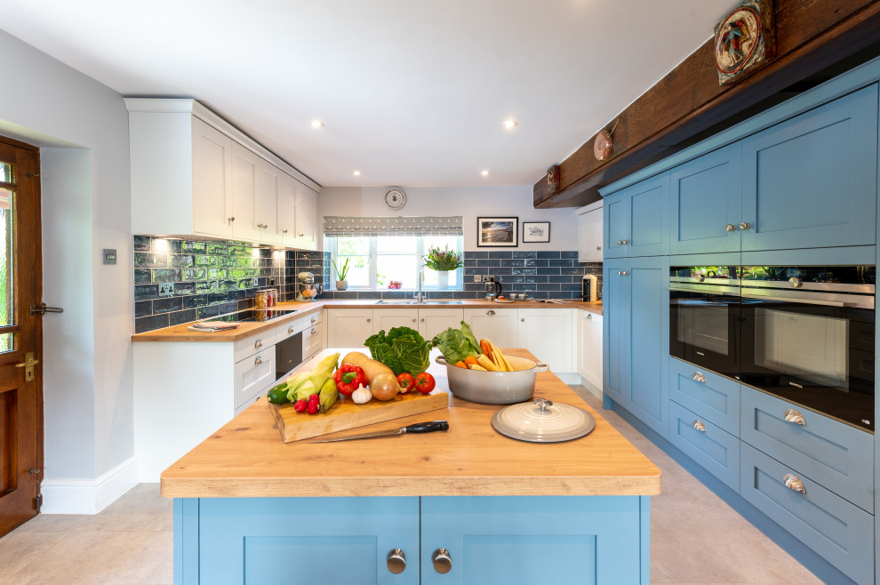 This is an example of a medium sized farmhouse u-shaped kitchen/diner in Surrey with a built-in sink, shaker cabinets, blue cabinets, laminate countertops, blue splashback, ceramic splashback, stainless steel appliances, vinyl flooring, an island, grey floors, brown worktops and exposed beams.