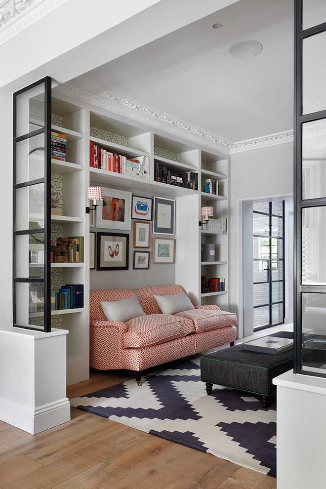 Transitional living room in London with a library, grey walls and light hardwood floors.