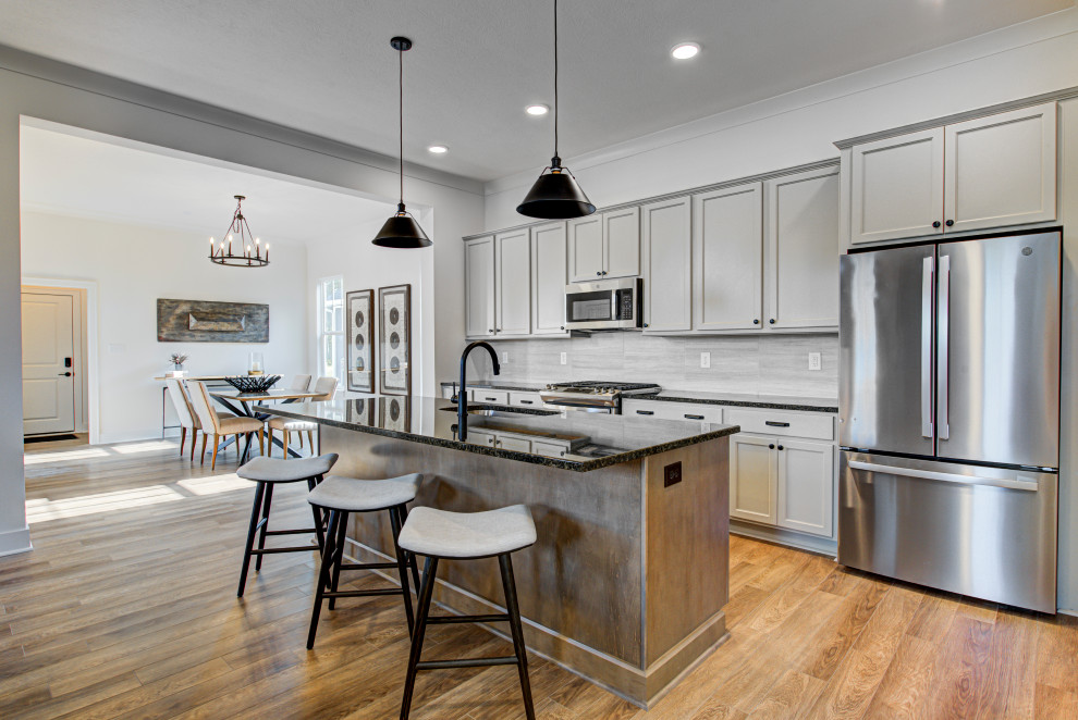 This is an example of a mid-sized arts and crafts galley eat-in kitchen in Indianapolis with with island, grey splashback, stainless steel appliances, vinyl floors, brown floor, black benchtop, an undermount sink, granite benchtops, shaker cabinets, beige cabinets and ceramic splashback.