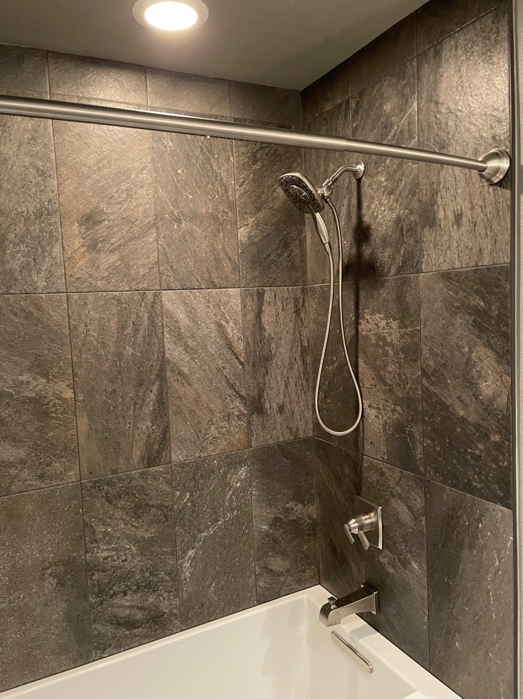 Bild på ett mellanstort funkis svart svart badrum för barn, med luckor med infälld panel, vita skåp, ett badkar i en alkov, en dusch/badkar-kombination, en toalettstol med separat cisternkåpa, brun kakel, porslinskakel, grå väggar, klinkergolv i porslin, ett undermonterad handfat, granitbänkskiva, grått golv och dusch med duschdraperi