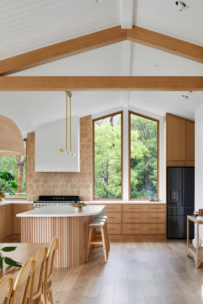 Inspiration for a large modern u-shaped open plan kitchen in Melbourne with a farmhouse sink, shaker cabinets, medium wood cabinets, pink splashback, porcelain splashback, black appliances, medium hardwood floors, with island, brown floor, white benchtop and exposed beam.