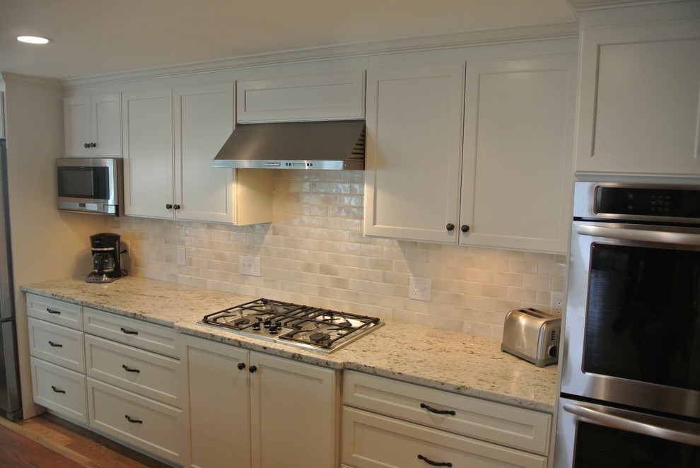 Example of a transitional galley light wood floor eat-in kitchen design in Boston with an undermount sink, stainless steel appliances, an island, shaker cabinets, white cabinets, wood countertops, white backsplash, ceramic backsplash and brown countertops
