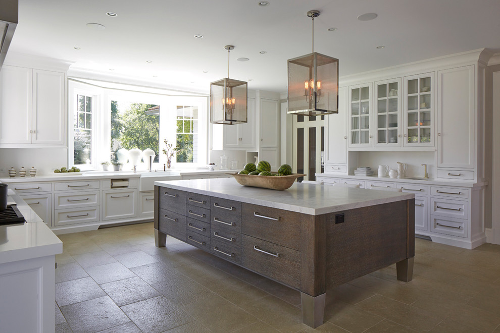 This is an example of a large transitional u-shaped kitchen in New York with a farmhouse sink, white cabinets, white splashback, with island, marble benchtops, travertine floors, beige floor and recessed-panel cabinets.