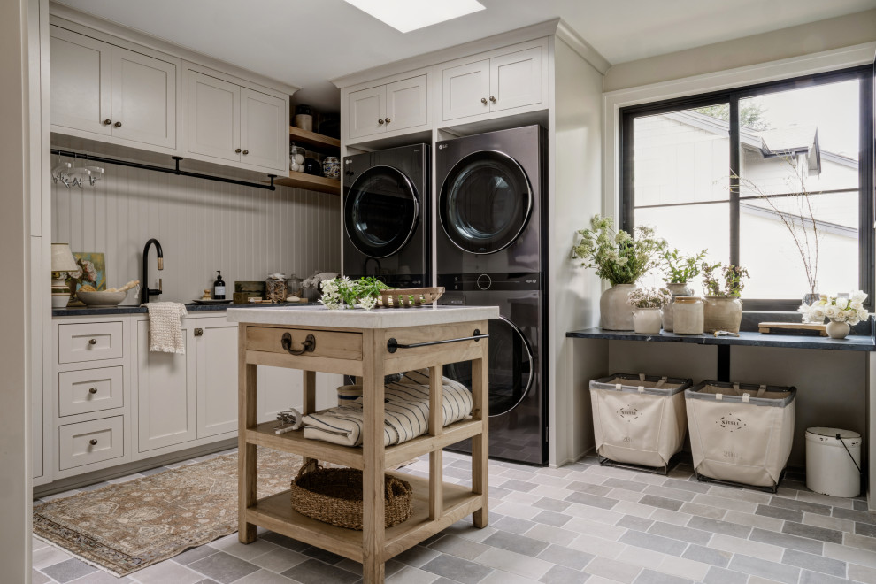 Transitional l-shaped gray floor dedicated laundry room photo in Seattle with an undermount sink, shaker cabinets, beige cabinets, white backsplash, shiplap backsplash, beige walls, a side-by-side washer/dryer and gray countertops