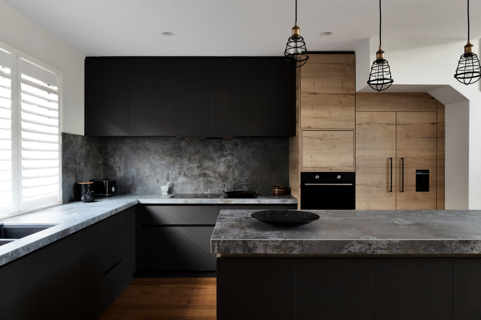 Design ideas for a mid-sized industrial l-shaped eat-in kitchen in Perth with black cabinets, grey splashback, black appliances, medium hardwood floors, with island, grey benchtop, a drop-in sink, solid surface benchtops and porcelain splashback.