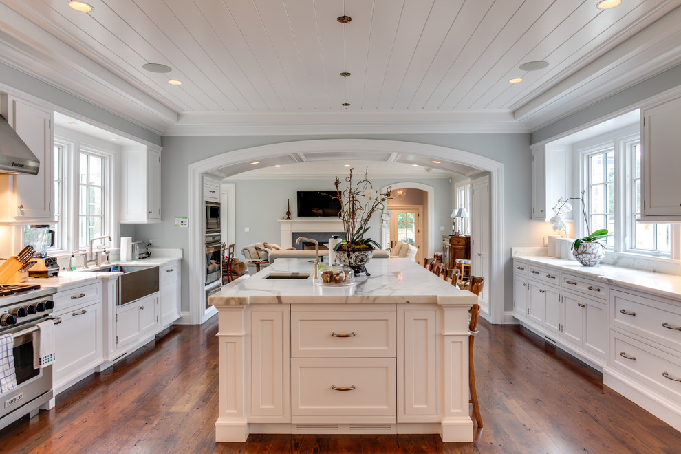 Inspiration for an expansive traditional u-shaped open plan kitchen in Other with a farmhouse sink, recessed-panel cabinets, white cabinets, stainless steel appliances, with island, brown floor, marble benchtops, white splashback, marble splashback and medium hardwood floors.