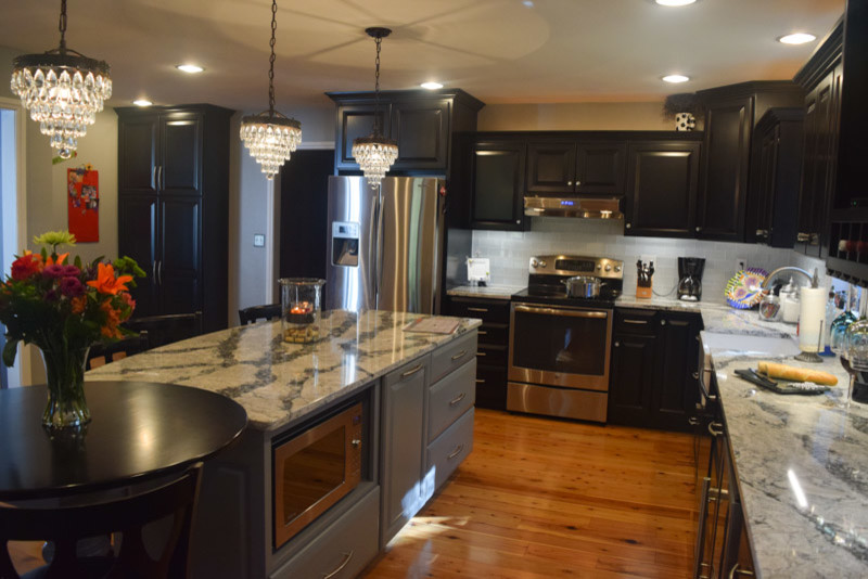 Example of a transitional medium tone wood floor kitchen design in Chicago with a farmhouse sink, raised-panel cabinets, black cabinets, quartz countertops, white backsplash, glass tile backsplash, stainless steel appliances and an island