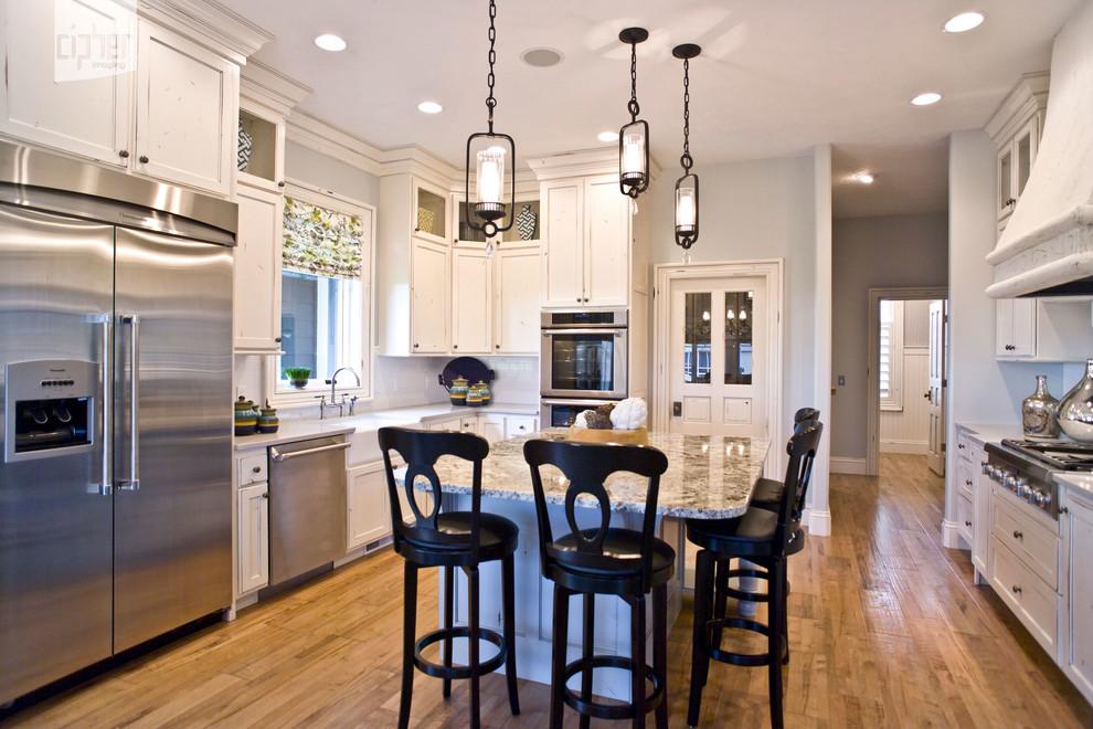 Inspiration for a mid-sized transitional u-shaped light wood floor and brown floor kitchen pantry remodel with stainless steel appliances, beige walls, an island, a farmhouse sink, raised-panel cabinets, distressed cabinets, granite countertops, white backsplash and subway tile backsplash
