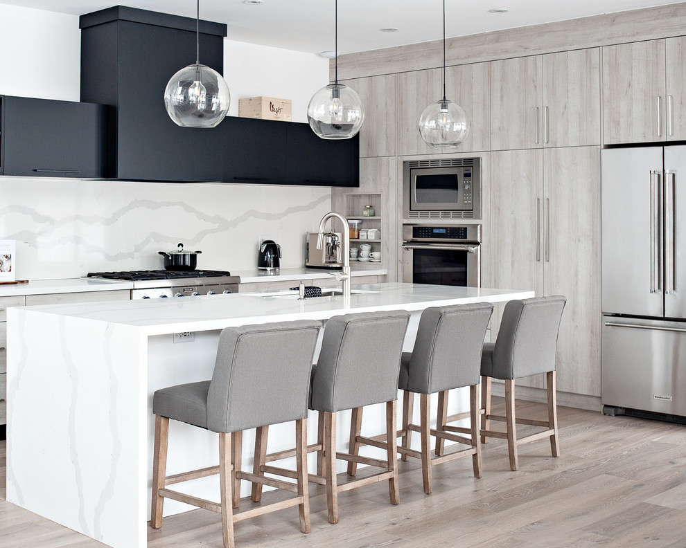 Trendy light wood floor and beige floor kitchen photo in Toronto with an undermount sink, flat-panel cabinets, white backsplash, stone slab backsplash, stainless steel appliances, an island, white countertops and beige cabinets