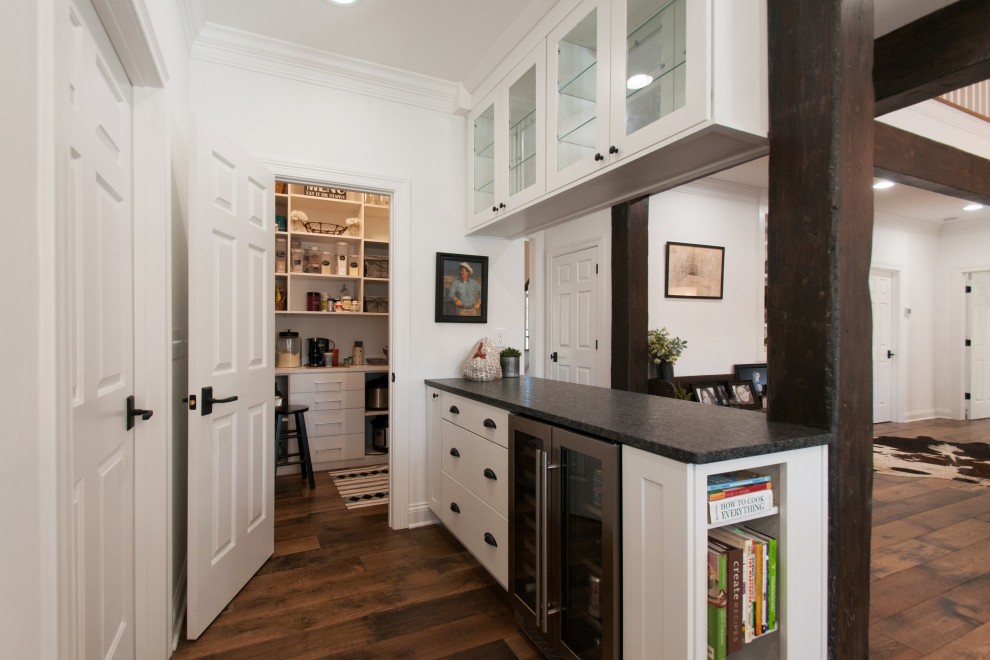 Inspiration for a small country galley home bar in Nashville with shaker cabinets, white cabinets, granite benchtops, medium hardwood floors, brown floor and black benchtop.