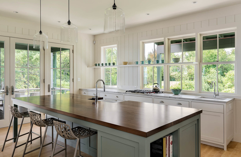 Mid-sized beach style galley eat-in kitchen in Portland Maine with a single-bowl sink, shaker cabinets, white cabinets, light hardwood floors, with island, wood benchtops, white splashback and stainless steel appliances.