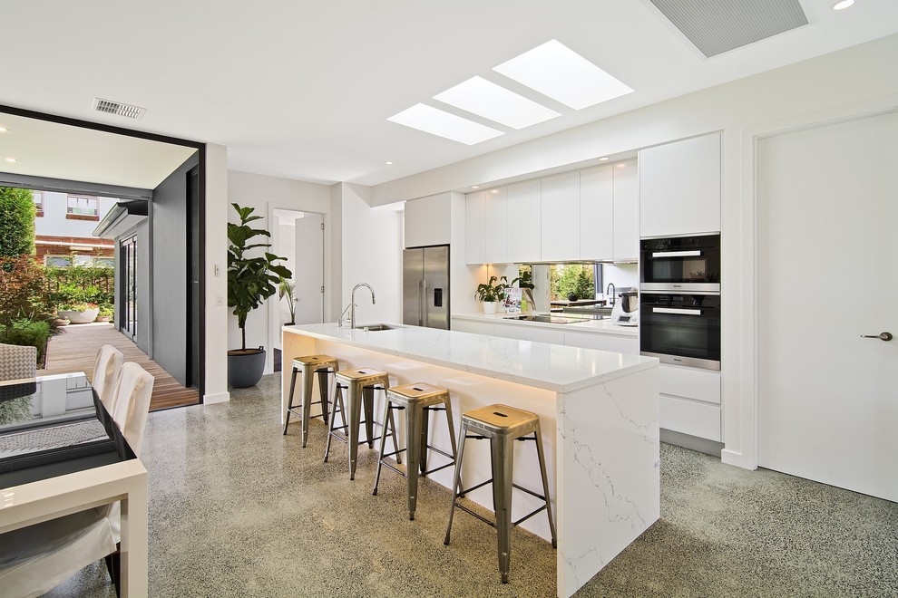 Photo of a contemporary galley open plan kitchen in Melbourne with an undermount sink, flat-panel cabinets, white cabinets, stainless steel appliances and with island.