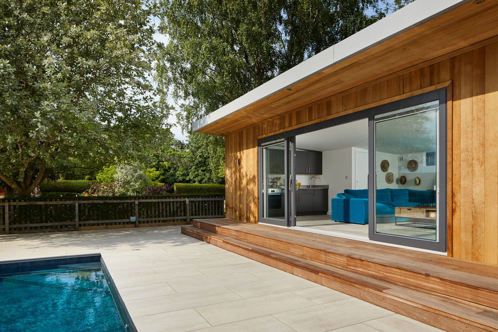 Contemporary backyard rectangular pool in Essex with a pool house and decking.