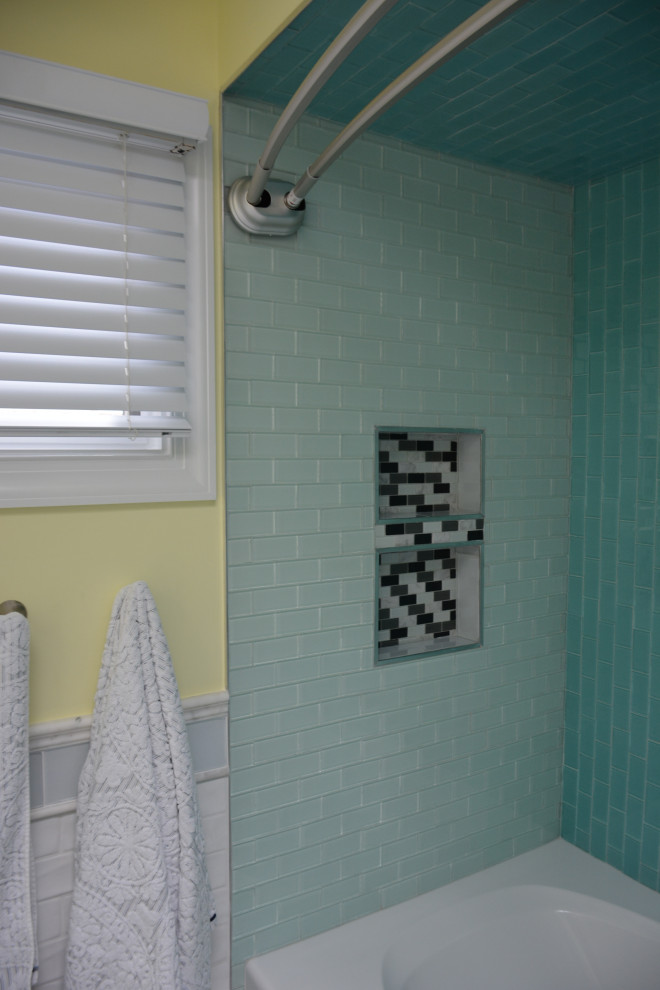 Mid-sized beach style kids bathroom in New York with raised-panel cabinets, green cabinets, an alcove tub, a shower/bathtub combo, a one-piece toilet, white tile, ceramic tile, yellow walls, ceramic floors, an undermount sink, marble benchtops, white floor, a shower curtain, white benchtops, a double vanity, a freestanding vanity and vaulted.
