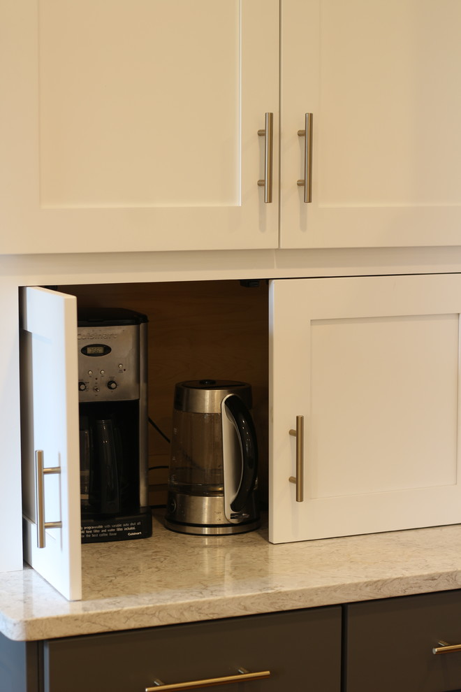 Example of a mid-sized transitional u-shaped medium tone wood floor and brown floor enclosed kitchen design with a farmhouse sink, shaker cabinets, white cabinets, quartz countertops, white backsplash, subway tile backsplash, white appliances, no island and beige countertops