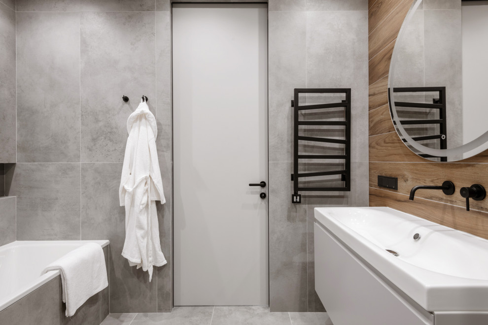 На фото: главная, серо-белая ванная комната среднего размера в современном стиле с плоскими фасадами, серыми фасадами, ванной в нише, душем в нише, инсталляцией, серой плиткой, керамогранитной плиткой, серыми стенами, полом из керамогранита, подвесной раковиной, серым полом, душем с раздвижными дверями, белой столешницей, зеркалом с подсветкой, тумбой под одну раковину и подвесной тумбой