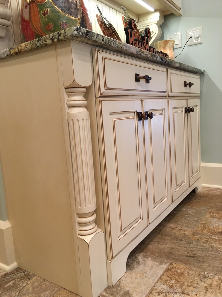 Inspiration for a large transitional galley porcelain tile enclosed kitchen remodel with an undermount sink, raised-panel cabinets, distressed cabinets, granite countertops, beige backsplash, stone tile backsplash, stainless steel appliances and a peninsula