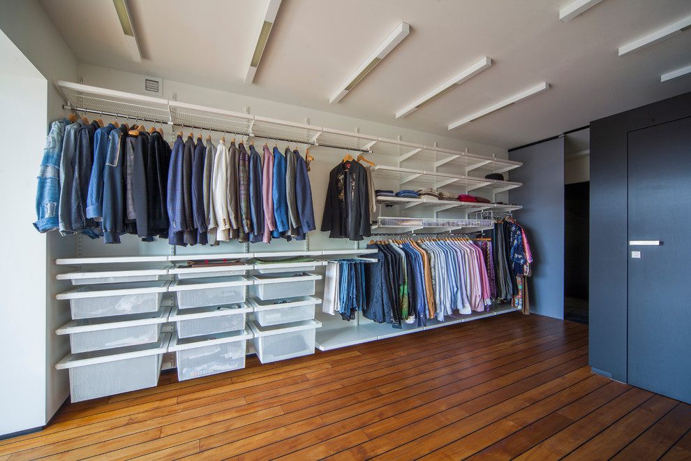Photo of an expansive contemporary men's walk-in wardrobe in Moscow with open cabinets, dark hardwood floors, brown floor and white cabinets.