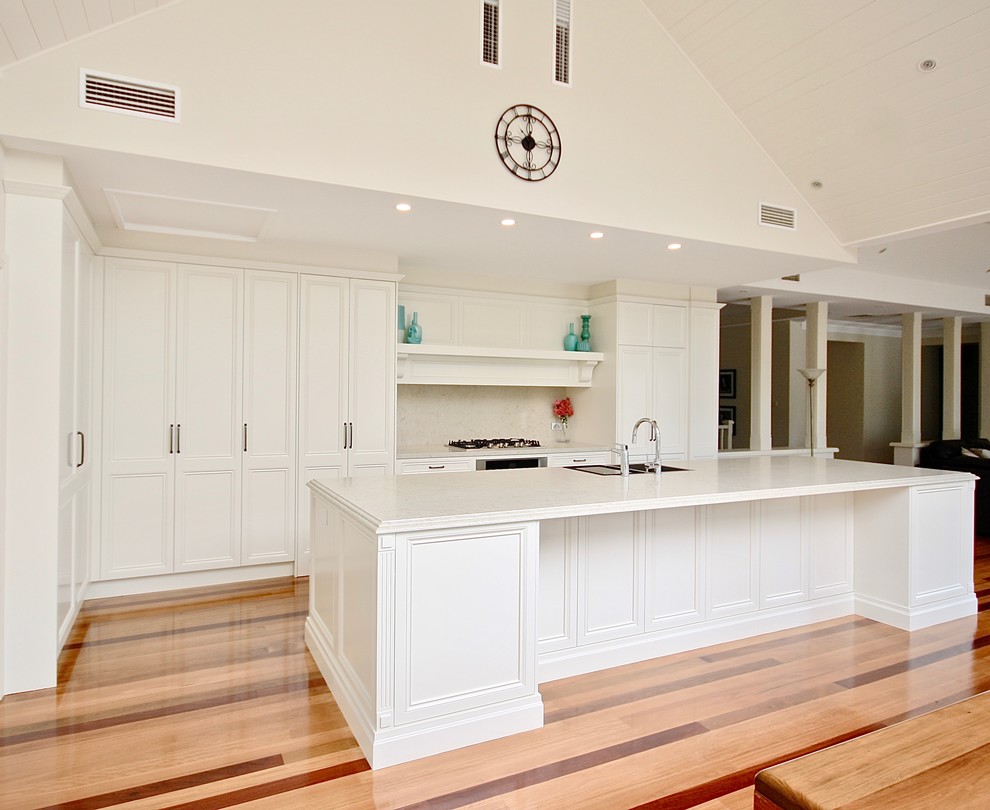 Design ideas for a large transitional l-shaped open plan kitchen in Sydney with a drop-in sink, recessed-panel cabinets, white cabinets, quartz benchtops, beige splashback, stone slab splashback, stainless steel appliances, medium hardwood floors and with island.