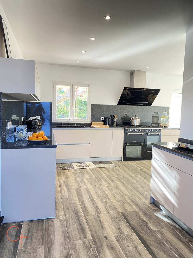 Inspiration for a large modern l-shaped open plan kitchen in Other with a double-bowl sink, flat-panel cabinets, beige cabinets, granite benchtops, black splashback, granite splashback, panelled appliances, ceramic floors, grey floor and black benchtop.