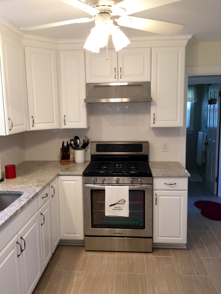 Example of a mid-sized u-shaped porcelain tile enclosed kitchen design with a peninsula, raised-panel cabinets, white cabinets, granite countertops, white backsplash, subway tile backsplash, stainless steel appliances and an undermount sink