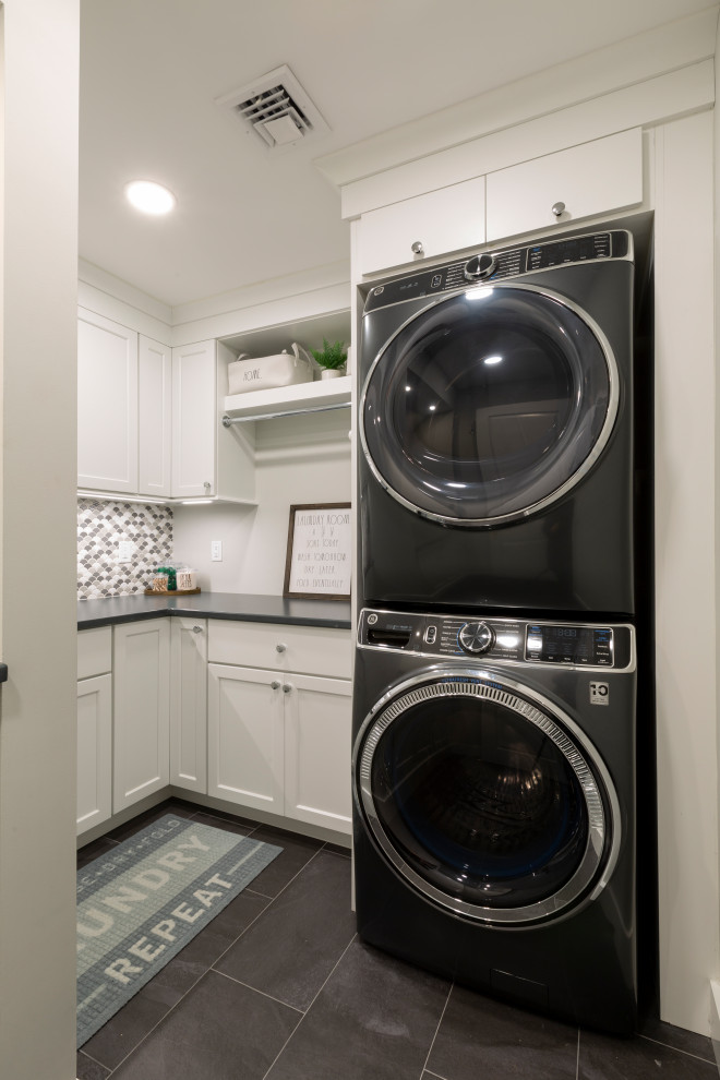 This is an example of a mid-sized transitional l-shaped dedicated laundry room in New York with an undermount sink, shaker cabinets, white cabinets, quartz benchtops, multi-coloured splashback, mosaic tile splashback, beige walls, a stacked washer and dryer and black benchtop.