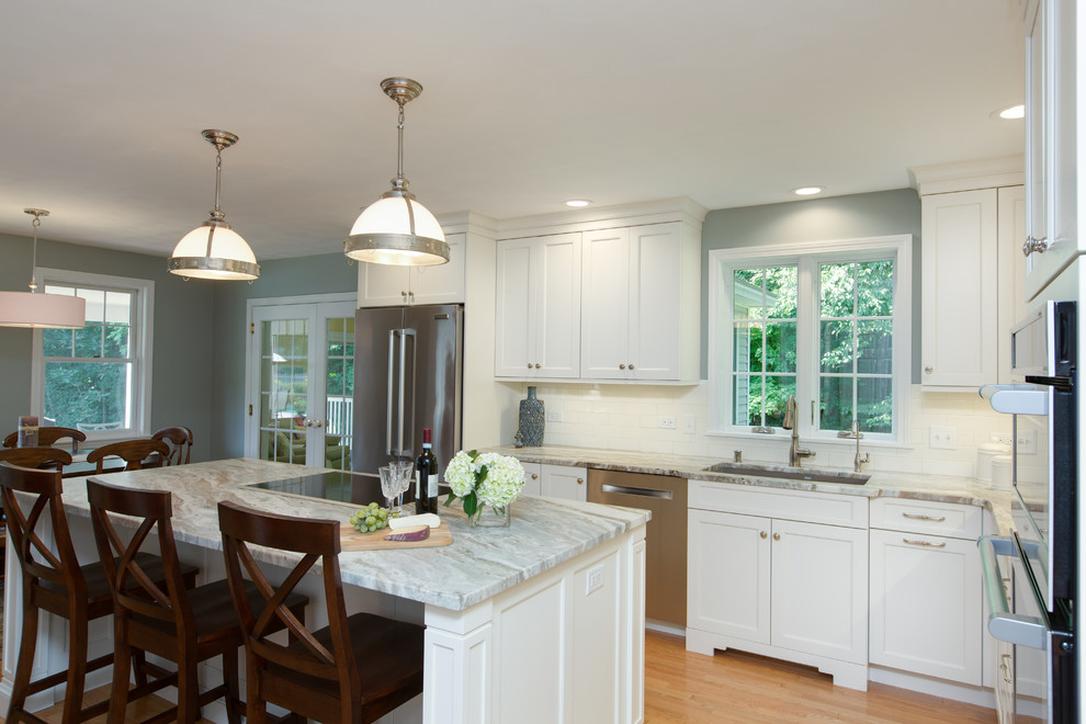 Example of a transitional l-shaped light wood floor eat-in kitchen design in Boston with an undermount sink, recessed-panel cabinets, white cabinets, quartzite countertops, white backsplash, subway tile backsplash, stainless steel appliances and an island
