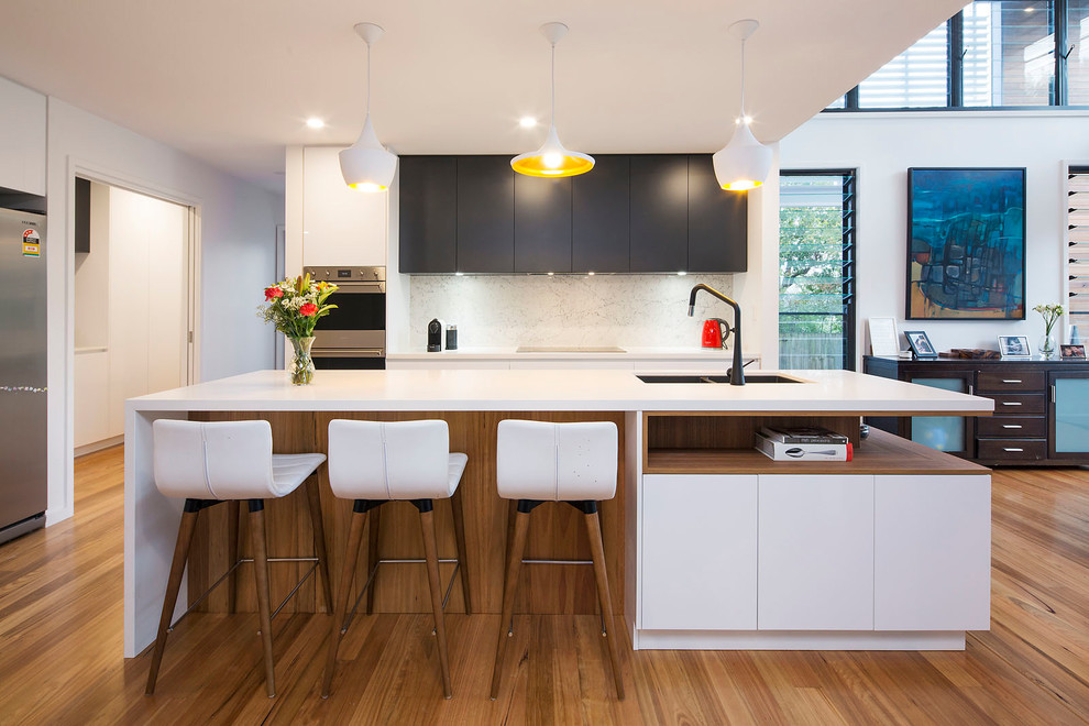 Inspiration for a mid-sized contemporary l-shaped open plan kitchen in Brisbane with a double-bowl sink, quartz benchtops, stainless steel appliances, medium hardwood floors, with island, flat-panel cabinets, black cabinets, white splashback, stone slab splashback and brown floor.