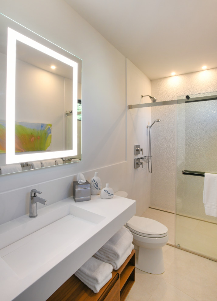 На фото: ванная комната, совмещенная с туалетом среднего размера в современном стиле с фасадами островного типа, душем без бортиков, белой плиткой, белыми стенами, душевой кабиной, раковиной с несколькими смесителями, душем с раздвижными дверями, тумбой под одну раковину, подвесной тумбой и любой отделкой стен