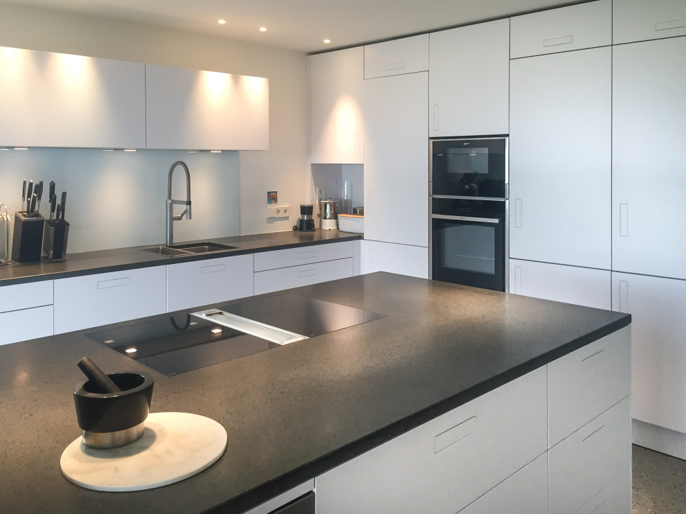 Design ideas for a mid-sized contemporary kitchen in Other with a double-bowl sink, flat-panel cabinets, white cabinets, granite benchtops, white splashback, black appliances, concrete floors, with island, grey floor and black benchtop.