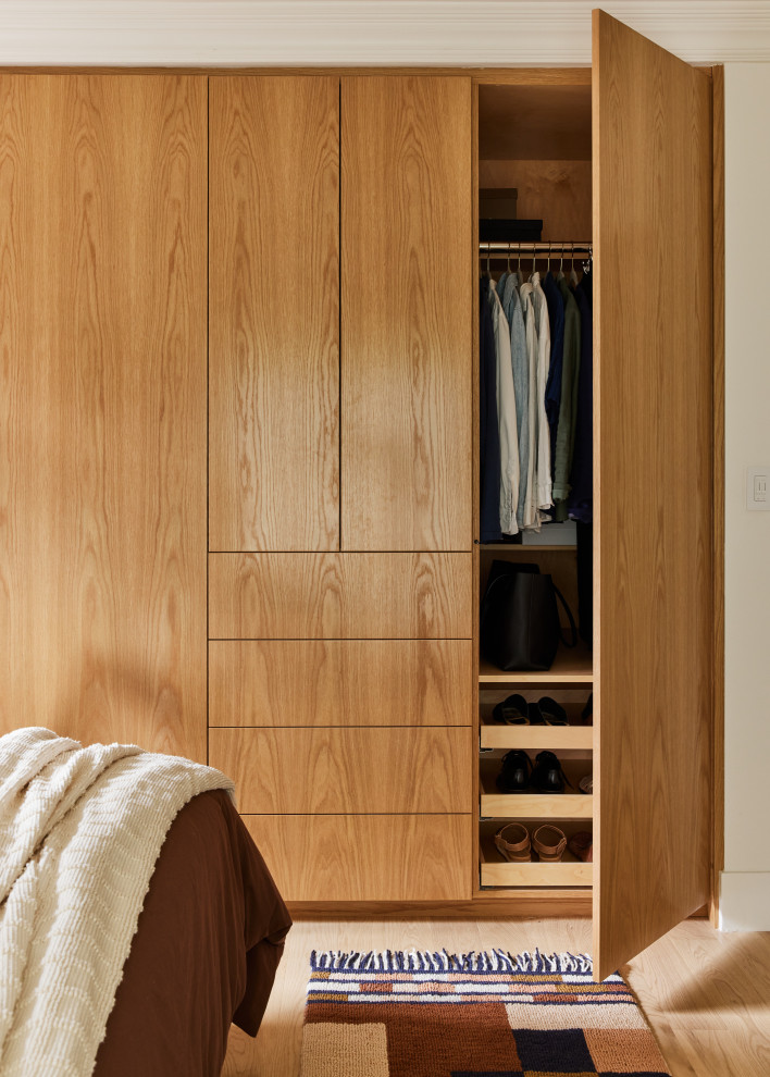 Diseño de armario y vestidor actual de tamaño medio con armarios con paneles lisos, puertas de armario de madera clara y suelo de madera clara