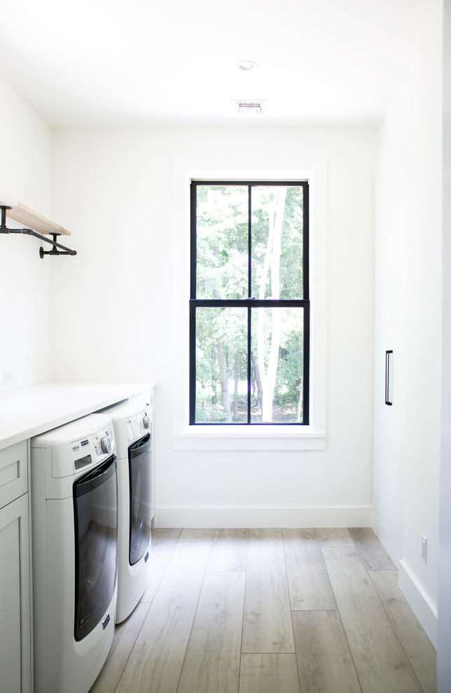 Photo of a mid-sized scandinavian galley dedicated laundry room in New York with an undermount sink, shaker cabinets, white cabinets, quartz benchtops, white walls, vinyl floors, a side-by-side washer and dryer and white benchtop.