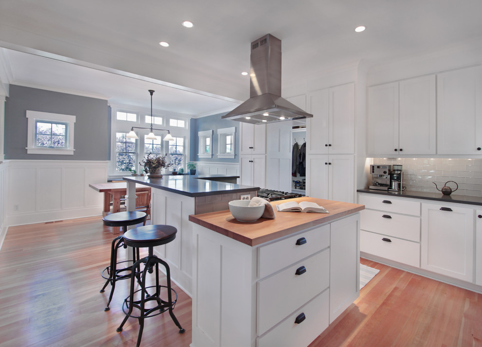 Photo of a mid-sized arts and crafts l-shaped eat-in kitchen in Seattle with wood benchtops, shaker cabinets, white cabinets, white splashback, glass tile splashback, an undermount sink, stainless steel appliances, medium hardwood floors, with island, brown floor and grey benchtop.
