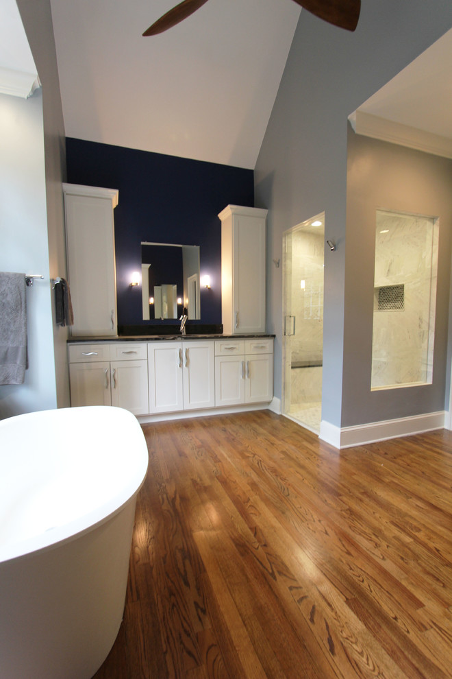 Photo of a large transitional bathroom in Atlanta with shaker cabinets, white cabinets, a freestanding tub, a two-piece toilet, black tile, black and white tile, gray tile, white tile, stone tile, blue walls, dark hardwood floors, an undermount sink, granite benchtops and with a sauna.